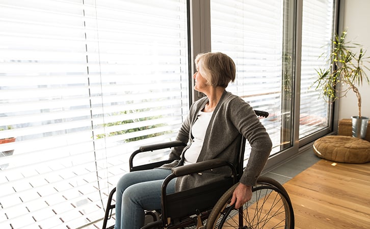 woman in wheelchair looking through blinds